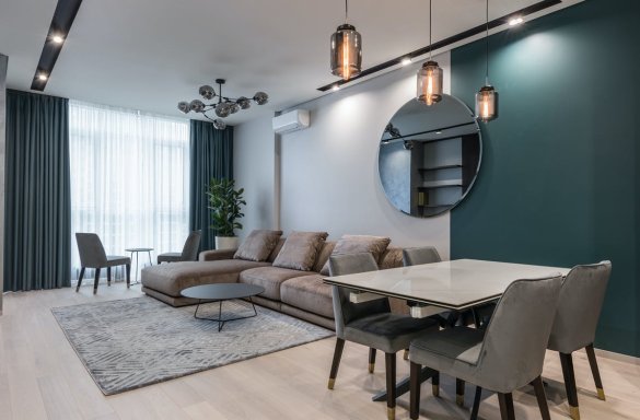 Interior of modern living room with comfortable big sofa and dining zone decorated with creative lamps and mirror in daylight