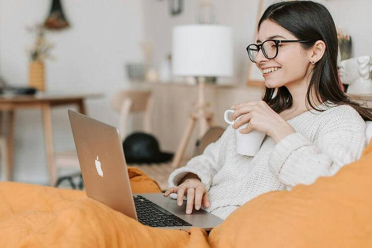 A happy woman using a laptop while holding a mug